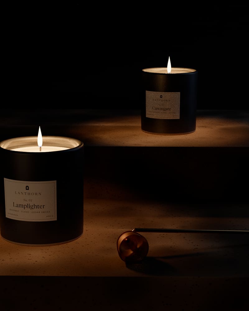 Lamplighter and Canongate candles on a worn sandstone step, lit, with a brass snuffer resting beside them in the dark.