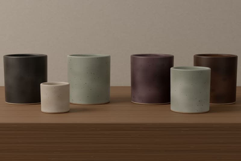 Empty stoneware vessels on an oak shelf in the four collection glazes, charcoal slate, pale grey-green haar, plum-grey heather and iron-brown peat, with a small bone-white votive.