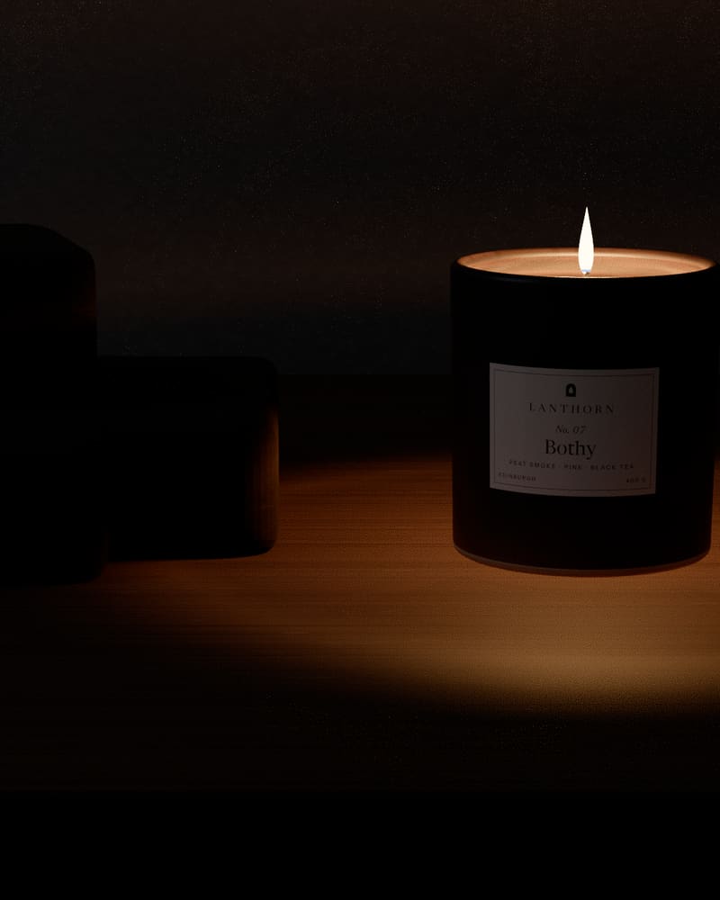 Bothy lit on a low oak bench beside a stack of dark peat bricks, in a dim room lit only by the candle.