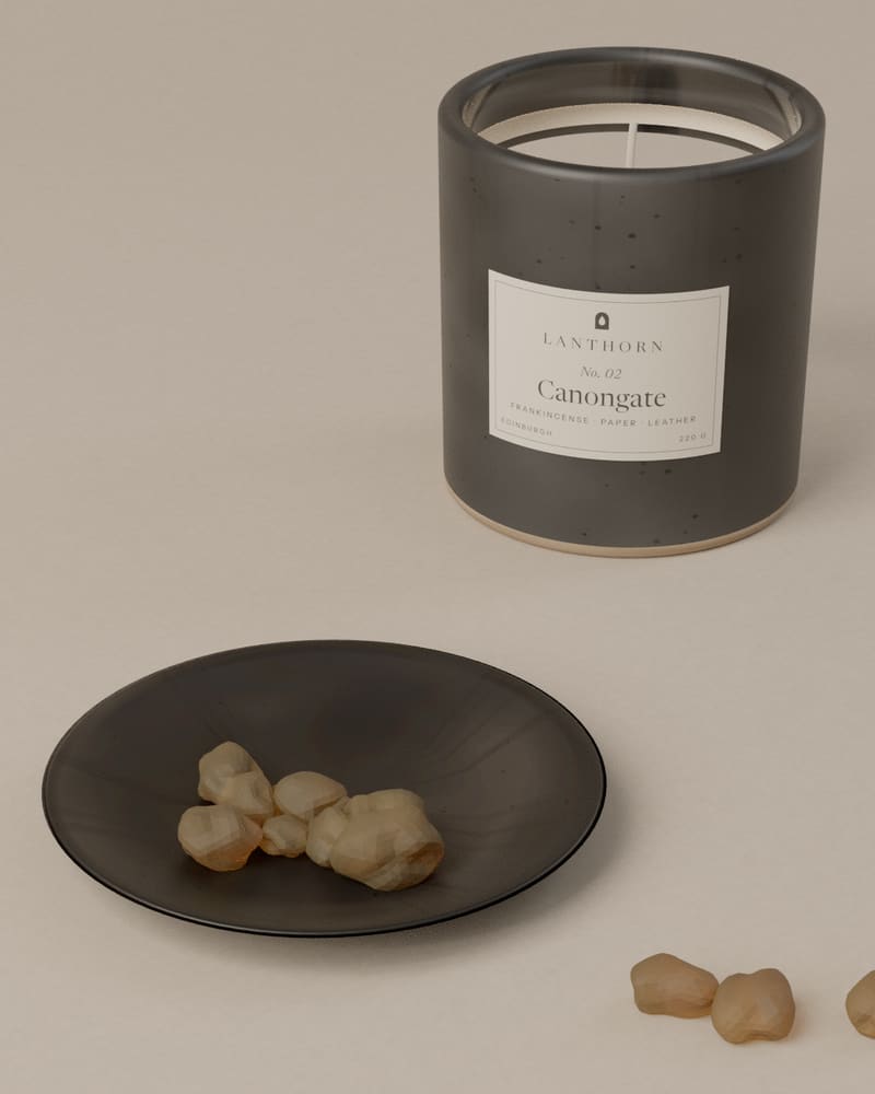 Pale gold frankincense resin tears in a small charcoal stoneware dish beside the Canongate candle.