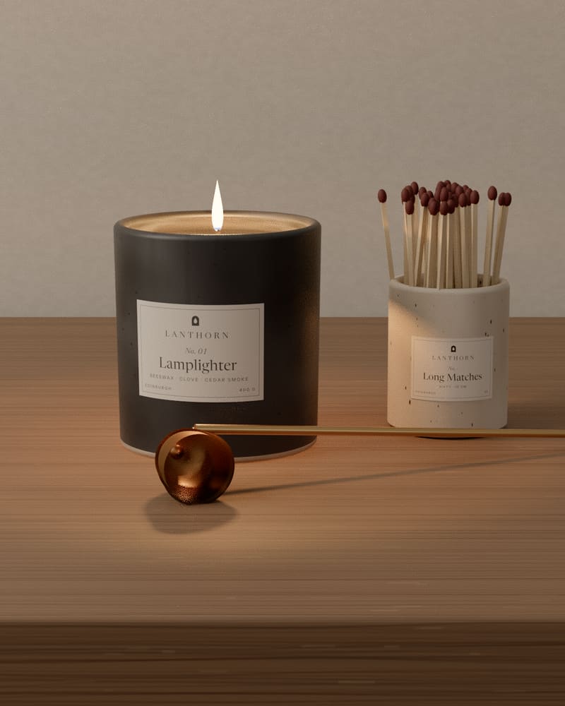 Lamplighter burning on an oak shelf against limewashed plaster, beside a brass snuffer and a jar of long matches.