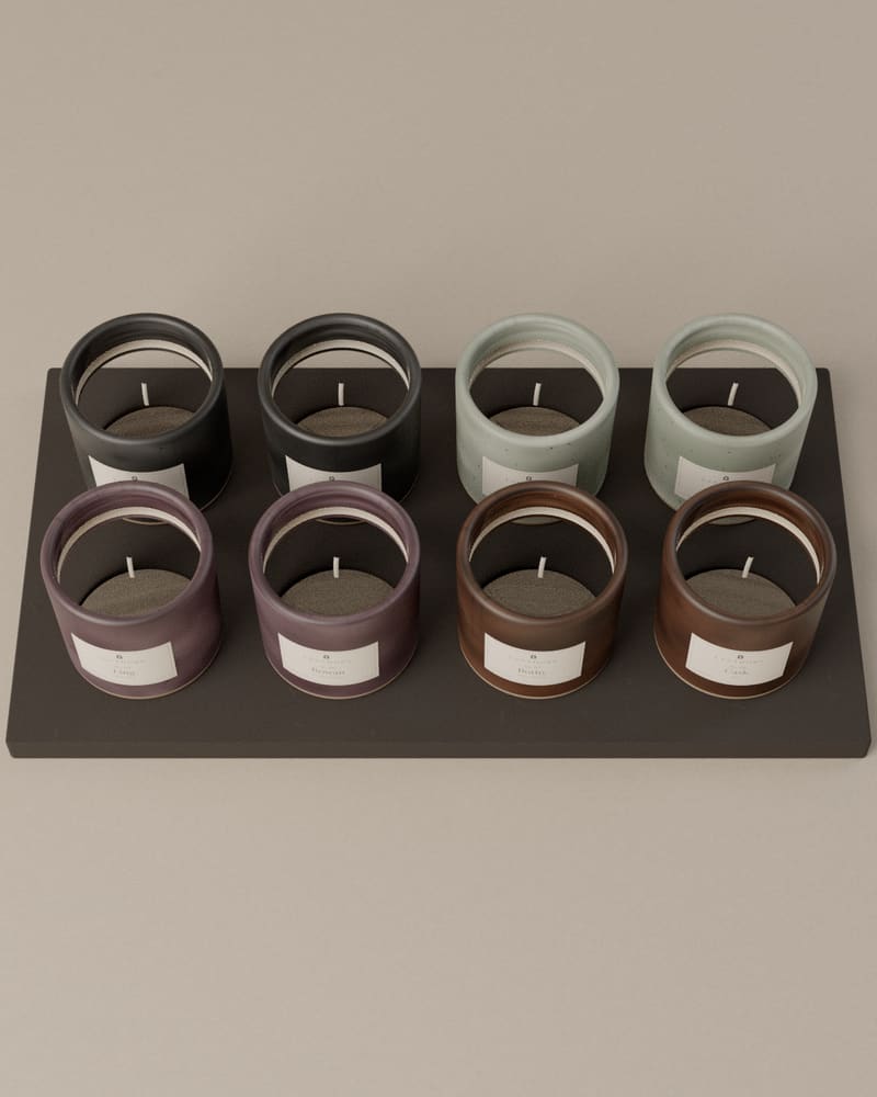 The Library Set: eight small stoneware votives in four glaze colours, standing in two rows on the charcoal tray of their box.