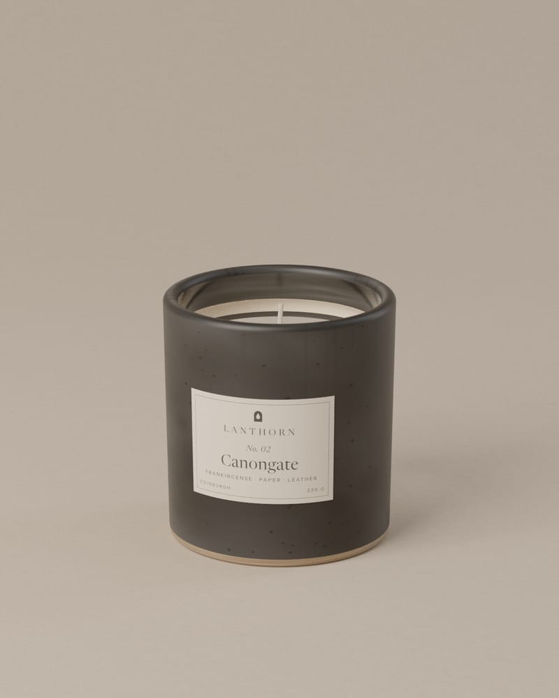 Canongate 220 g candle in charcoal speckled stoneware with its paper label, on a plain warm-grey backdrop.