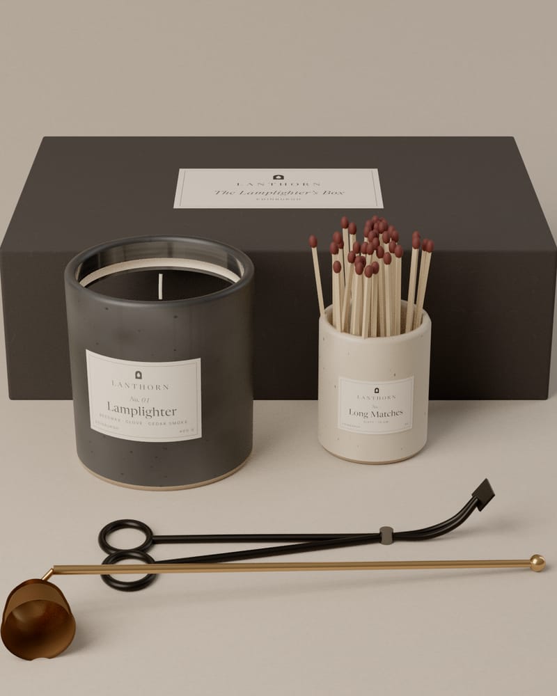 The Lamplighter’s Box: a charcoal gift box behind a Lamplighter candle, a stoneware jar of long matches, a blackened wick trimmer and a brass snuffer.