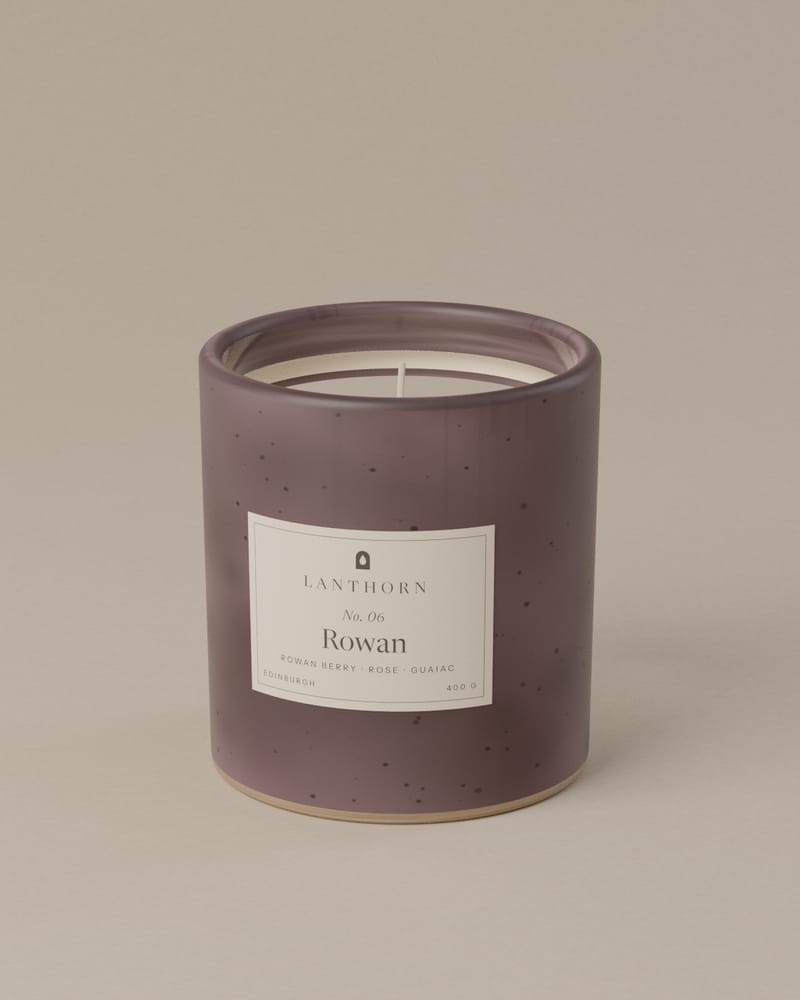 Rowan 400 g candle in plum-grey speckled stoneware with its paper label, on a plain warm-grey backdrop.